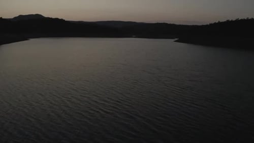 Calm clear water of Rumblar Reservoir during sunset on summer evening against dark silhouettes
