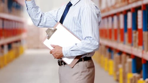 Male warehouse worker counting stocks and holding on clipboard