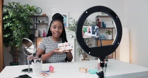 Artista de maquillaje experimentado de ascendencia afroamericana aplica sombra de ojos en los párpados grabando un