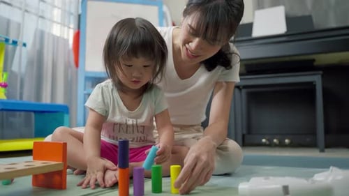 Asiatische glückliche Familie, schöne Mutter und kleines Mädchen spielen zusammen Spielzeug im heimischen Wohnzimmer