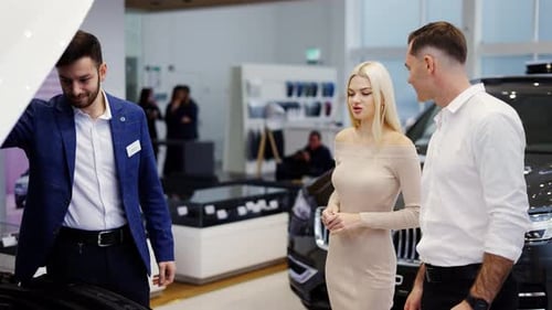 Salesman Showing Car Engine Under Open Hood to Couple in Auto Showroom