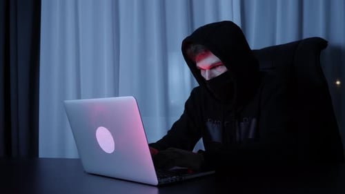 Man in black mask and hood sitting in dark room and hacking online social security protection