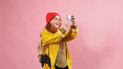 Studio Portrait of a Redheaded Happy Girl in a Yellow Raincoat Using a Smartphone