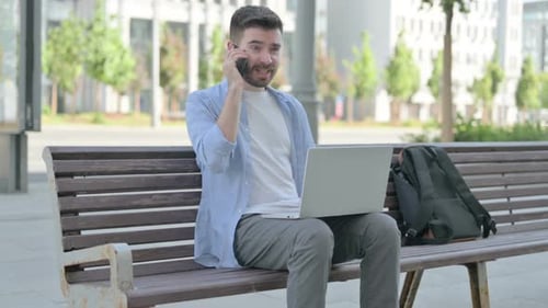 Young Man Talking on Phone While Working on Laptop