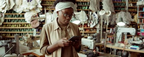 African American Woman Working on Tablet in Shoemaker Workshop