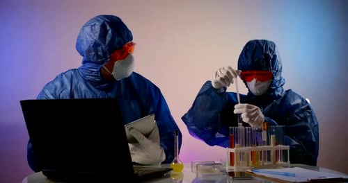 Las personas con ropa protectora con capuchas, respiradores, gafas y guantes se sientan en una mesa con un