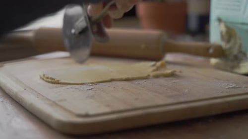 Up close view of two women using rolling cutter to make simple, homemade cookies on wooden cutting b