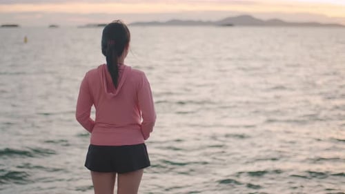 A beautiful Asian female runner looks at the sea view while standing on the beach.