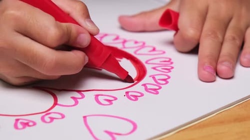 Close-up of a little girl drawing a heart and coloring with her colored markers.