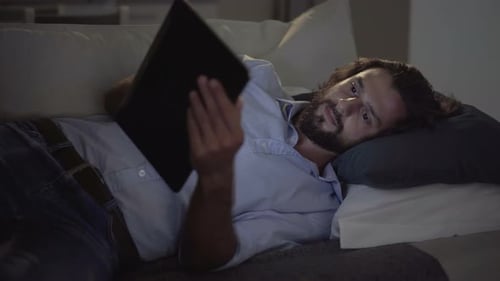 Man Lying in Bed with Tablet at Night