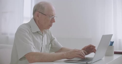 Senior Man Typing on Laptop at Desk Indoors