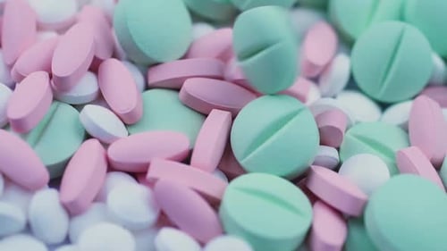 Round Green Pills Fall on White Vitamins and Pink Oval Antibiotics. Closeup