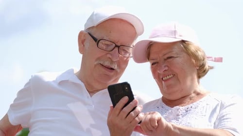 Modern Grandparents Use a Smartphone They Have Fun Sitting in a City Park
