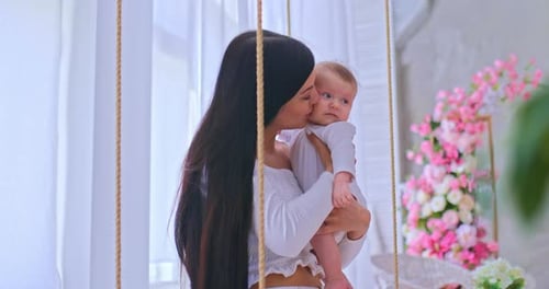 Woman Holds Baby in Flower-Decorated Indoor Swing