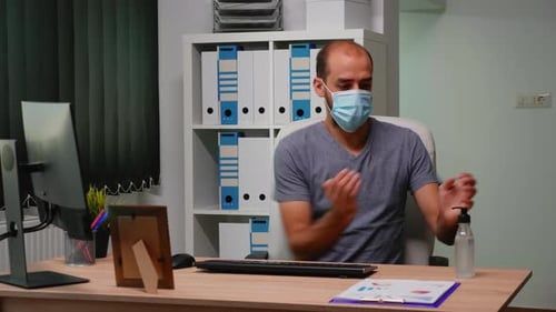 Man Wearing Mask Sanitizing Hands Before Typing