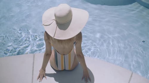 Woman in Swimsuit and Hat Sitting by Pool