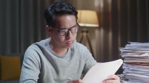 Close Up Of Tired Asian Man Shaking His Head While Working Hard With Documents At The Home