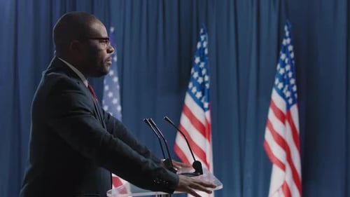 Man Speaking at Lectern with US Flags