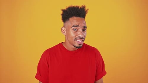 Close Up Portrait of Young Black Guy Trying to Hear you Putting Hand to Ear Orange Studio Background