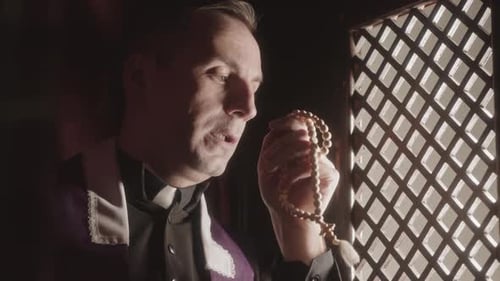 Priest with Rosary Beads Sitting in Confession Booth