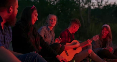 Picnic of Young People with Bonfire on the Beach in the Evening Cheerful Friends Singing Songs and