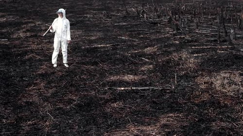 Scientist in Protective Suit Walking on Charred Landscape