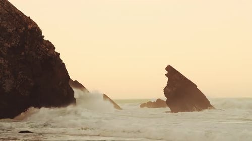 Wellen krachen gegen Felsen bei orangefarbenem Sonnenaufgang, wunderschöne zerklüftete felsige Küstenlandschaft und Küste