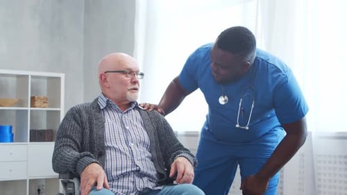 Healthcare Professional Comforts Mature Man in Wheelchair