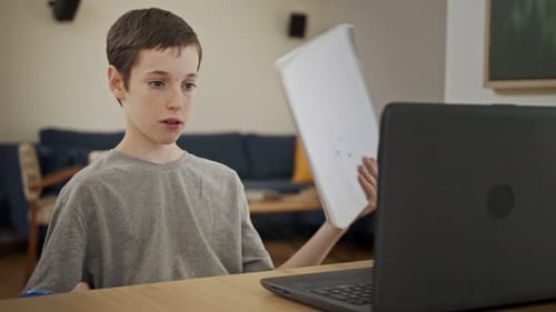Boy Working On A Laptop and Writing In Notebook