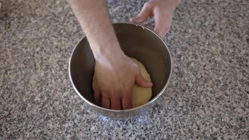 Placing a sourdough ball into a metal mixing bowl with some oil, the dough is turned in the oil befo