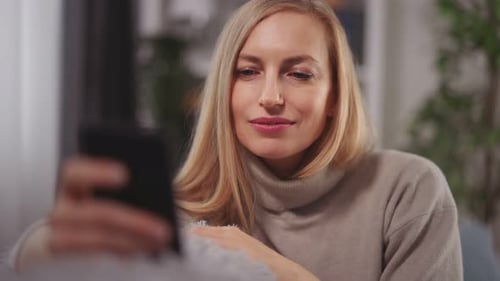 Woman Smiling While Using Her Smartphone at Home