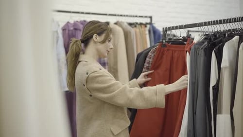 Side View Portrait of Beautiful Young Caucasian Woman Choosing Stylish Clothes in Shop. Confident