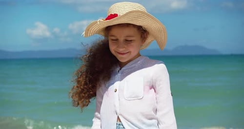Porträt eines lustigen kleinen Mädchens mit Hut Ein lächelndes Kind, das in die Kamera schaut, steht am Strand