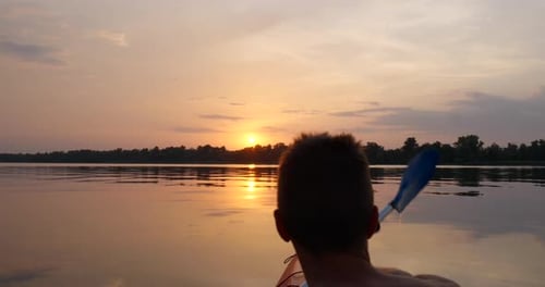 A Man Kayaks on a Calm River Towards the Sunset