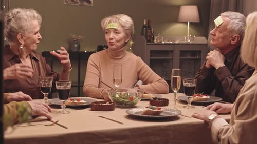 Seniors Playing Guessing Game Around Dinner Table