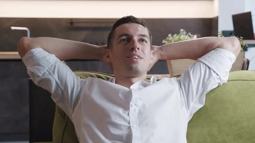 Man relaxing on sofa with hands behind head