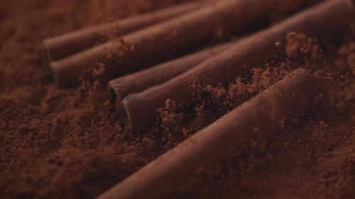 Cinnamon sticks falling into cinnamon powder. Slow Motion.