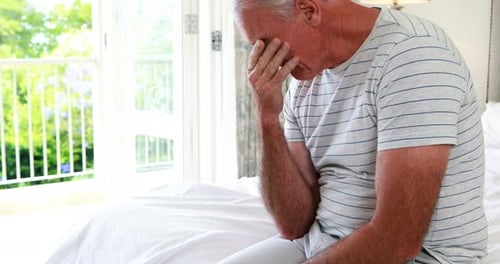 Worried senior man sitting on bed in bedroom