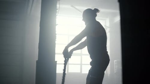 Man Exercising with Battle Ropes in Smoky Gym