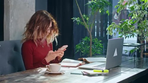 Happy Young Woman Sits with Phone and Computer at the Table