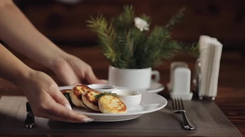 Hands of Waiter Puts Ceramic Plate with Delicious Pancakes with Jam on Table in Modern Restaurant