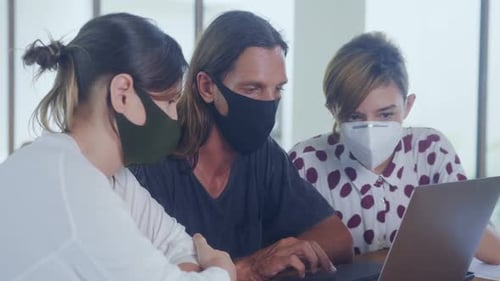 Colleagues collaborate on computer in office wearing masks