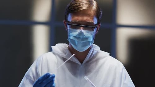 Kaukasischer männlicher medizinischer Mitarbeiter in Schutzkleidung und Gesichtsmaske untersucht Patientenabstrichtest