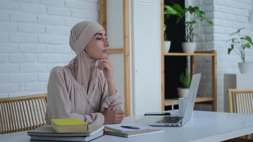 Young Woman Thoughtfully Working at Desk with Laptop