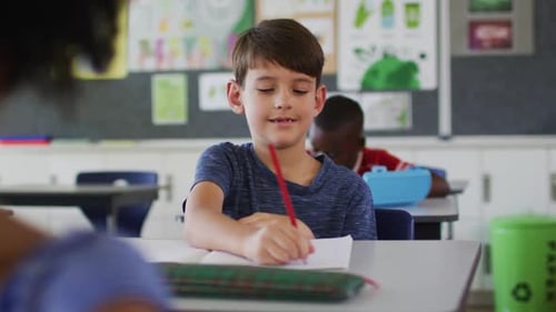Boy Writes at Desk in Classroom Setting