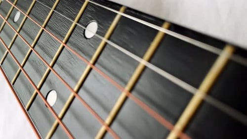 Zoomaufnahme einer akustischen Gitarrensaite mit schwarzen Bünden am Griffbrett