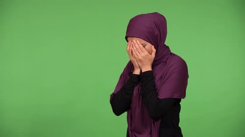 A Young Beautiful Muslim Woman Cries with Hands Covering Her Face Green Screen Background