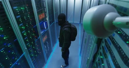 Maskierter Hacker mit seinem Laptop, der durch Serverreihen wacht
