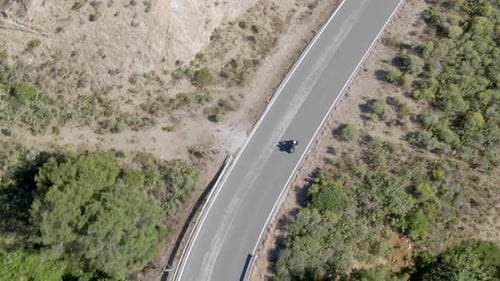 Tracking aerial shot of couple on motorbike on mountain road in summer