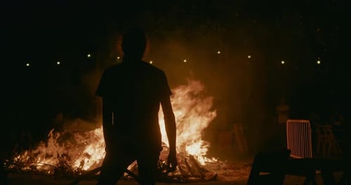 Silhouette Stares at Raging Bonfire at Night